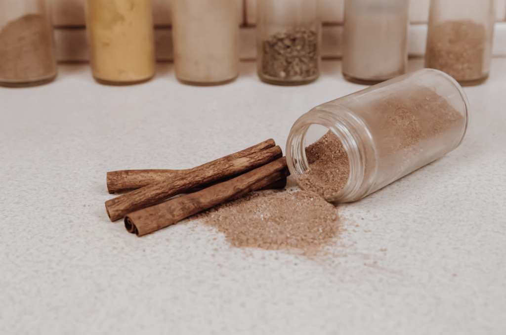 A jar of scattered cinnamon powder on a background of spices.