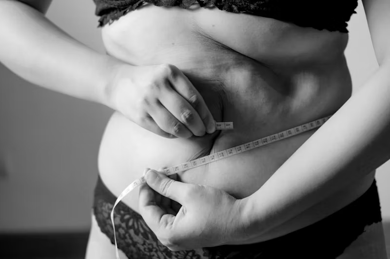 Grayscale photo of woman measuring her waist.