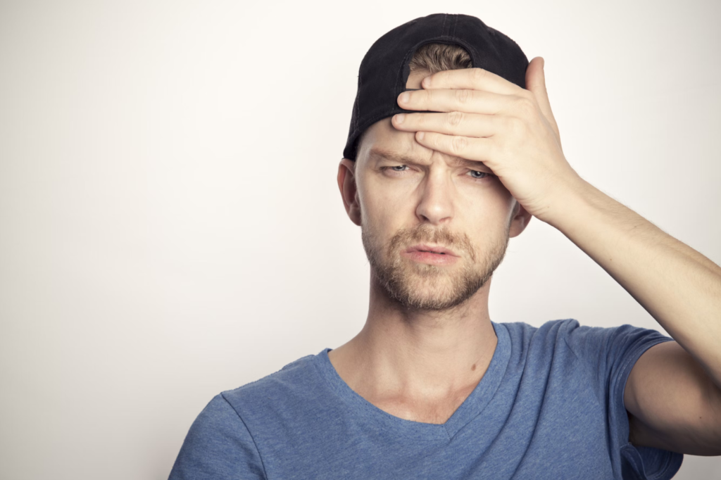 Man in a blue crew neck shirt holding his head. 