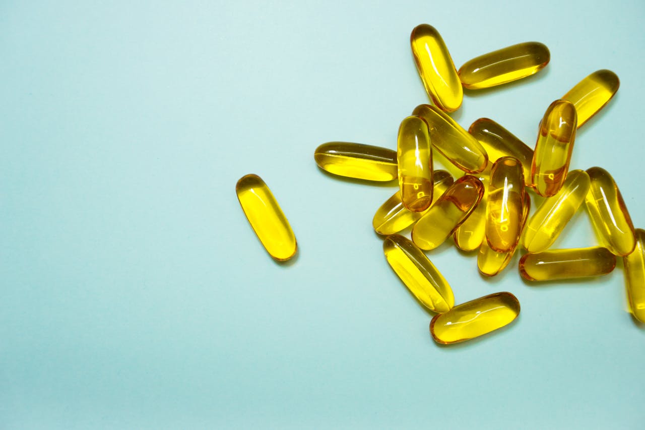 Close-up of yellow gel capsules scattered on light blue surface, representing dietary supplements or vitamins.