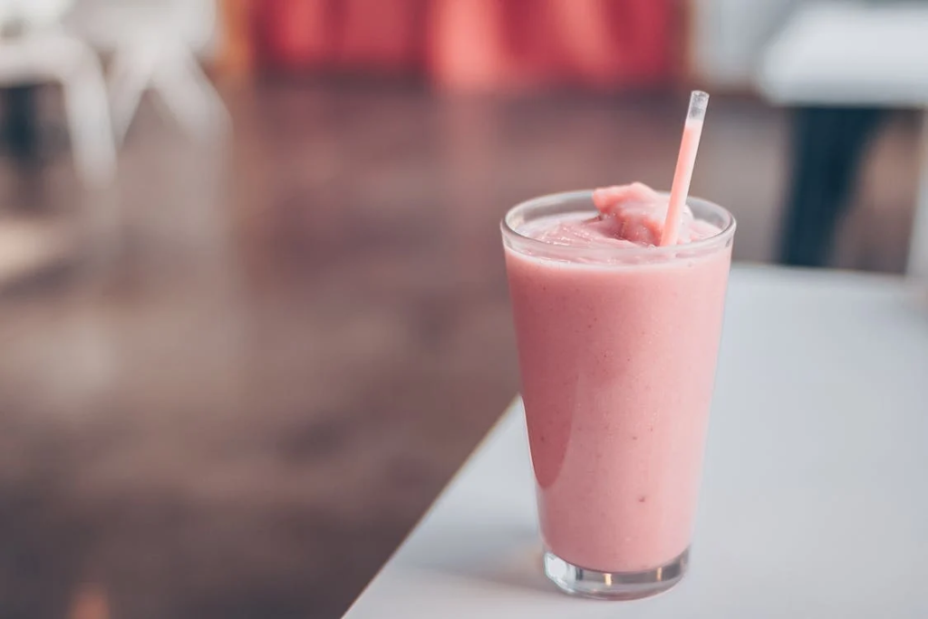 Glass filled with pink smoothie is placed on a white surface.