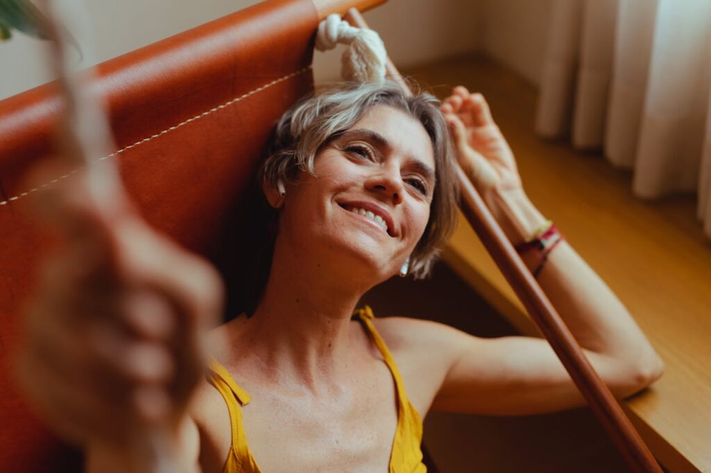 Middle-aged woman with short hair smiles while relaxing on a hammock indoors.