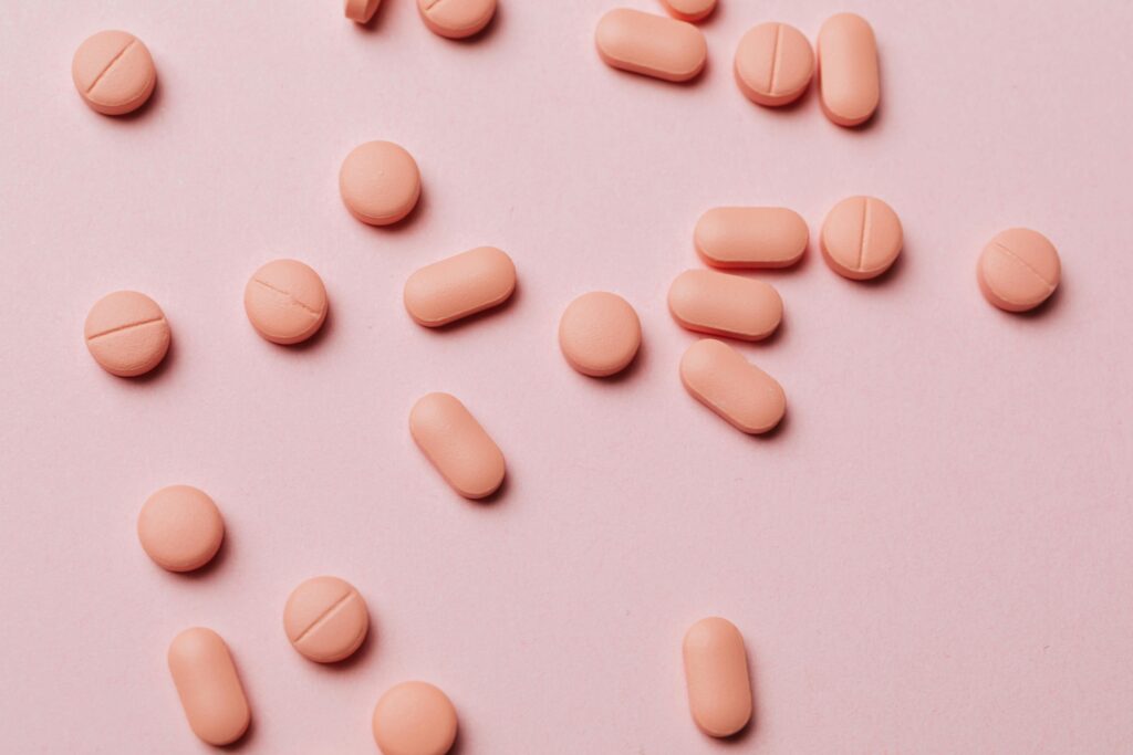 Scattered light pink tablets on pink surface, some round and others oblong.