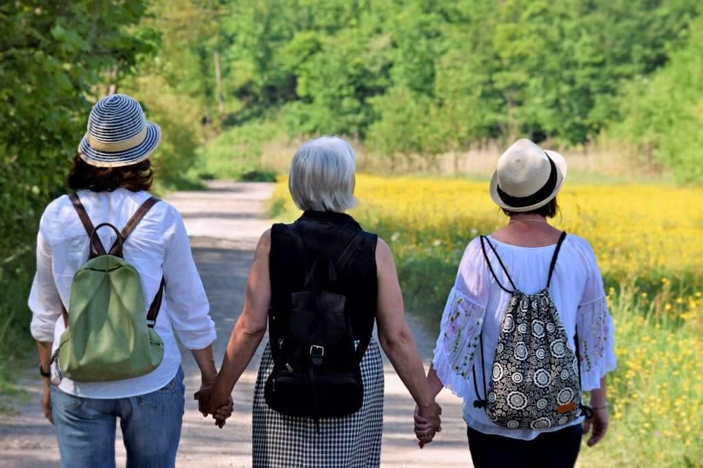 Three women walking hand in hand down a country path, enjoying a sunny day surrounded by nature.