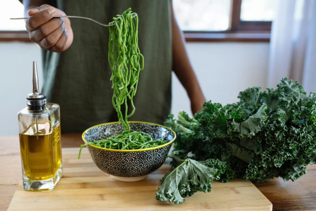 A person holding a fork with spinach pasta.