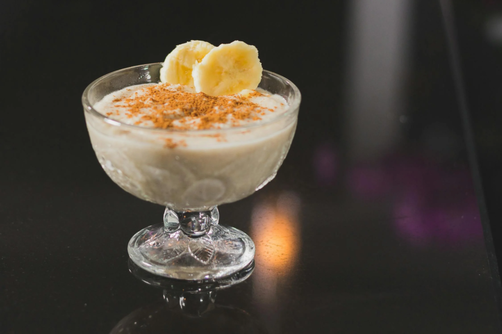 A close up photo of almond and banana smoothie in a glass cup.