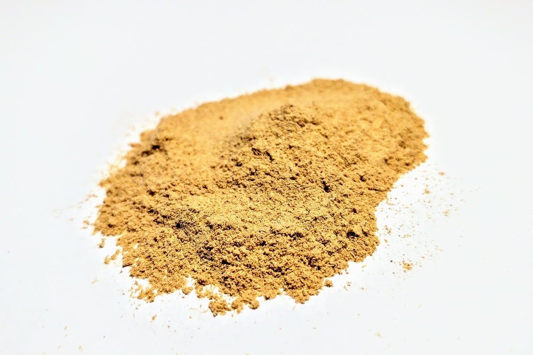 A close-up view of a small pile of light brown powder on a white surface.