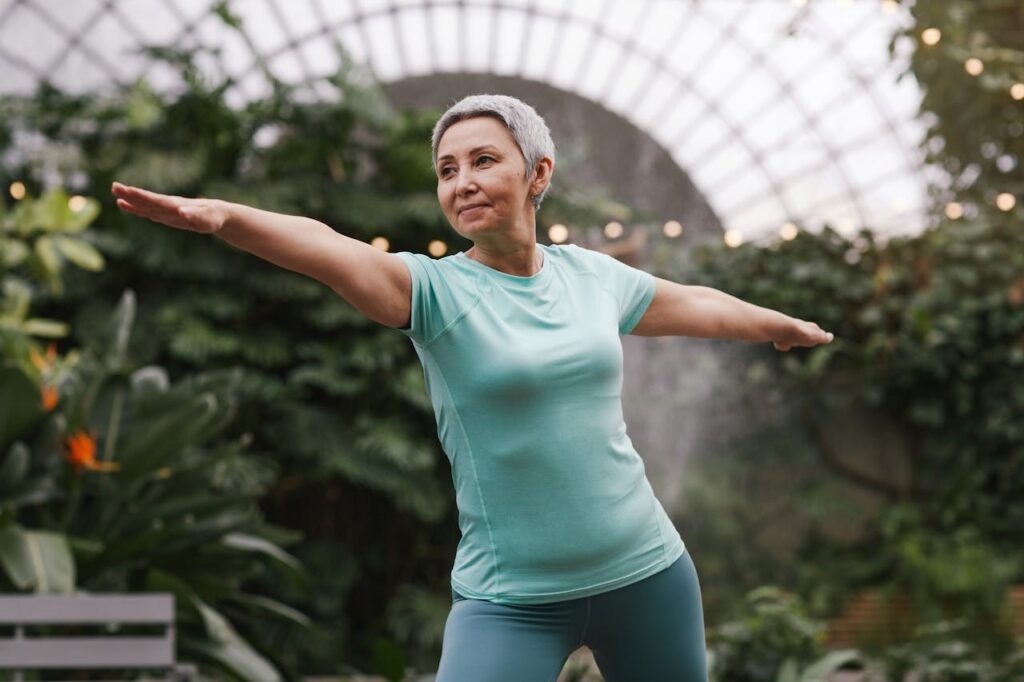 A mature woman in a light blue shirt practicing yoga outdoors.