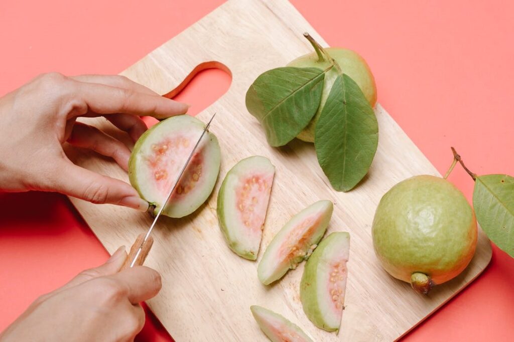 A person slicing a pink guava on a wooden cutting board.
