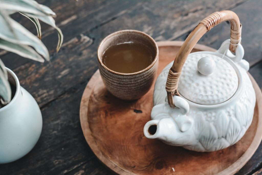 A rustic wooden tray holding a ceramic teapot with a cup of herbal tea on a dark wooden table.