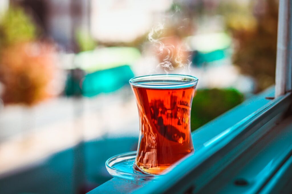 A steaming glass of tea placed on a windowsill, with blurred outdoor scenery in the background.