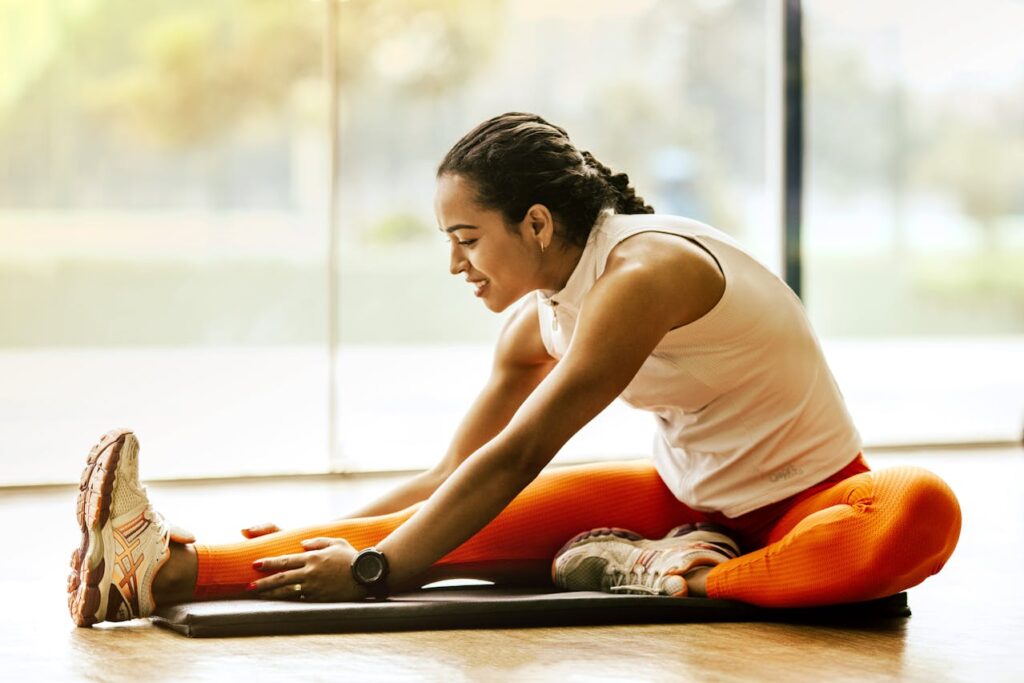 A woman in athletic wear stretching on a yoga mat in a sunlit room.