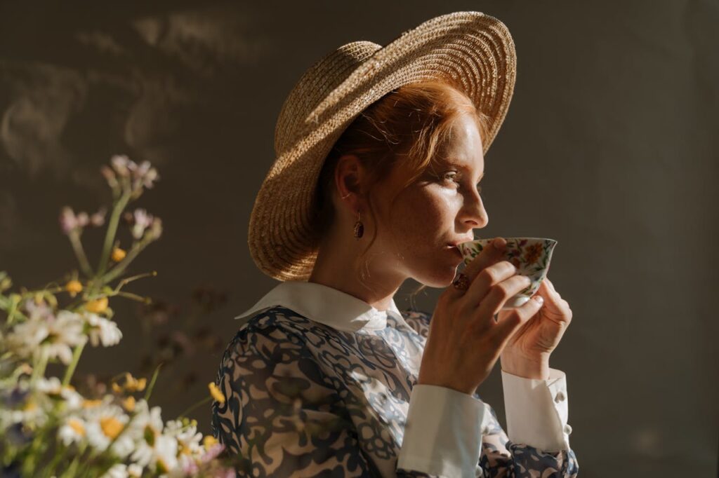 A woman wearing a straw hat sips a drink from a teacup.