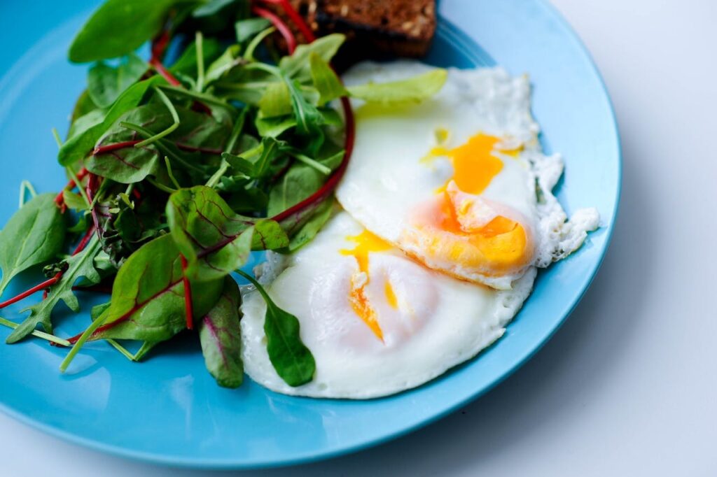 Breakfast with two fried eggs and fresh green salad leaves, served on a blue plate.