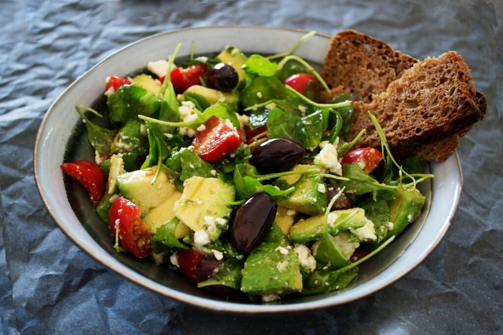 Fresh and colorful salad in a bowl, featuring avocado, cherry tomatoes, olives, leafy greens, and feta cheese.