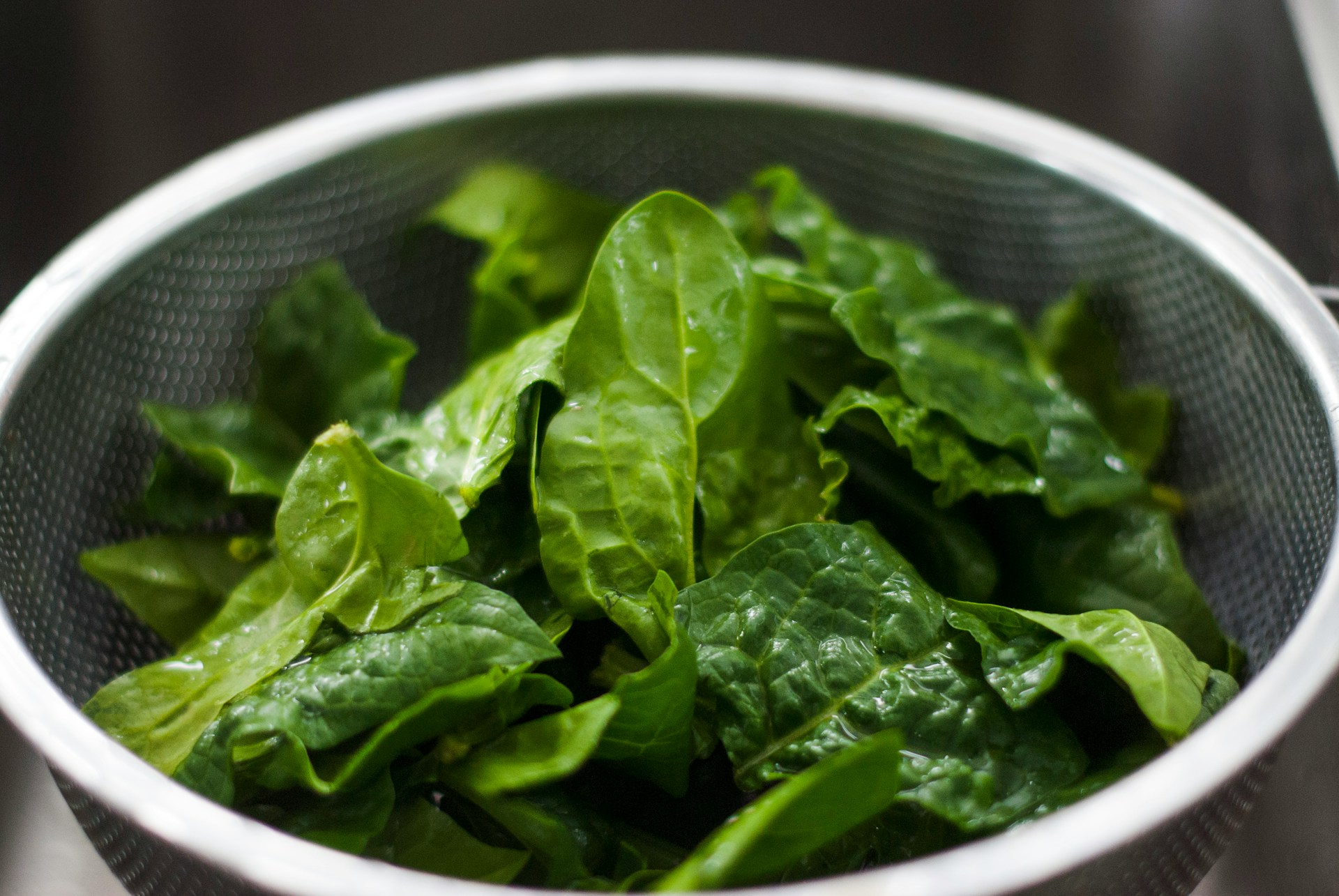 Fresh spinach leaves sitting in a metal colander, ready for washing or cooking.