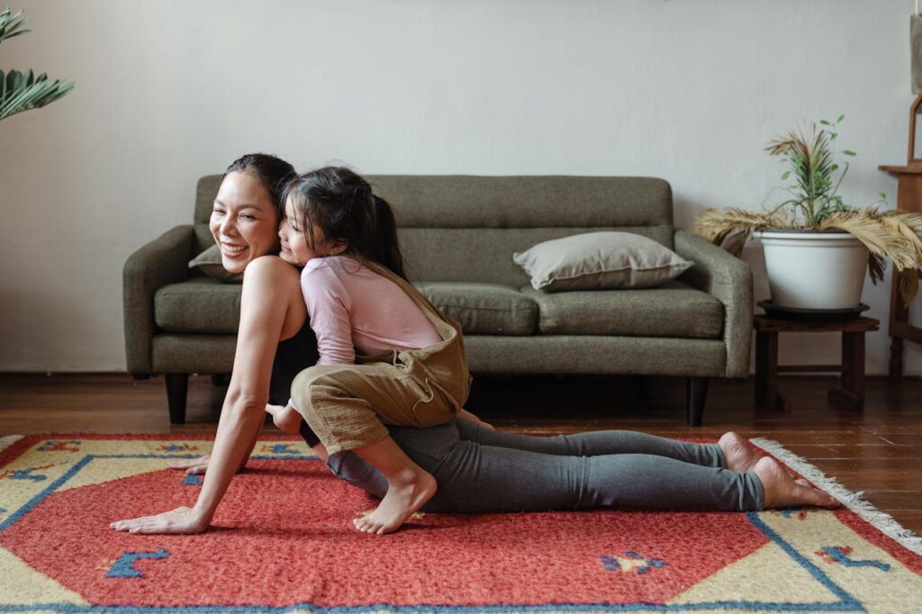 Smiling mother doing yoga with young daughter climbing on her back, enjoying a playful moment in the living room.