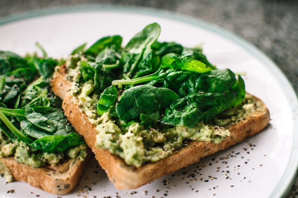 Toast topped with fresh spinach leaves on a white plate.