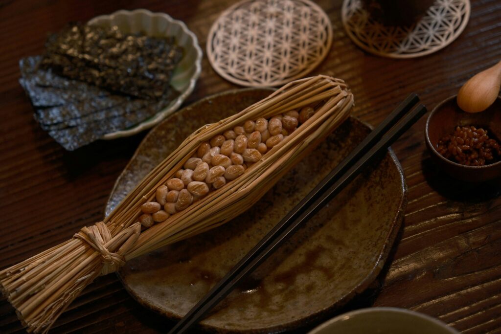 Traditional Japanese dish of fermented soybeans (natto) wrapped in straw, served with seaweed and other side dishes on a wooden table.
