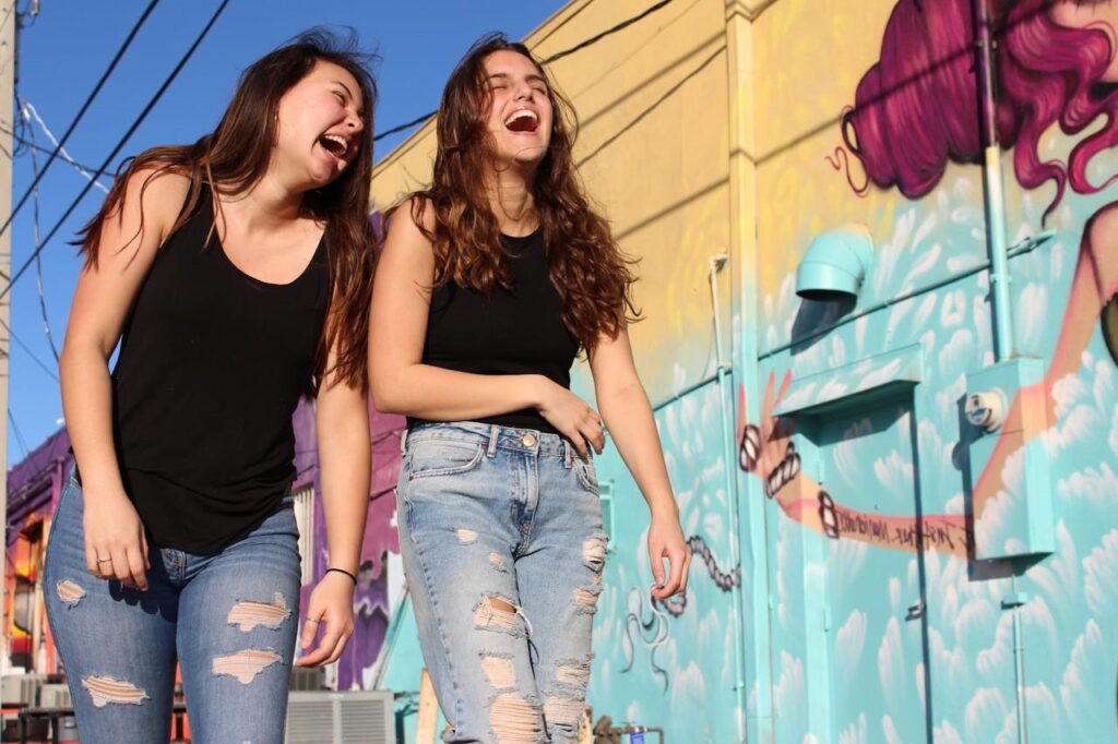 Two young women walking and laughing together in front of a colorful mural.