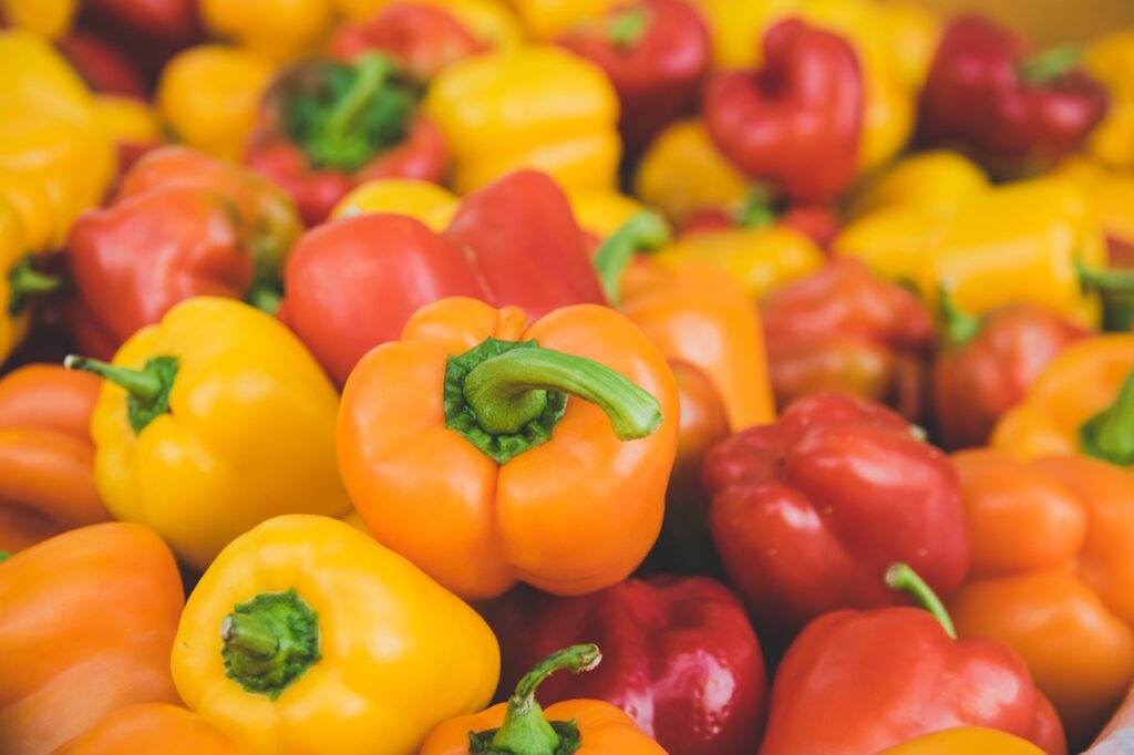A collection of fresh orange, yellow, and red bell peppers piled together.