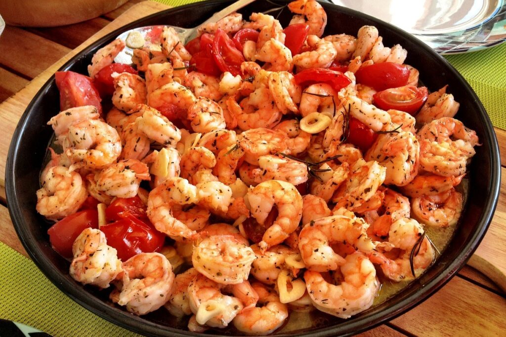 A large dish of cooked shrimp seasoned with herbs and served with sliced tomatoes.