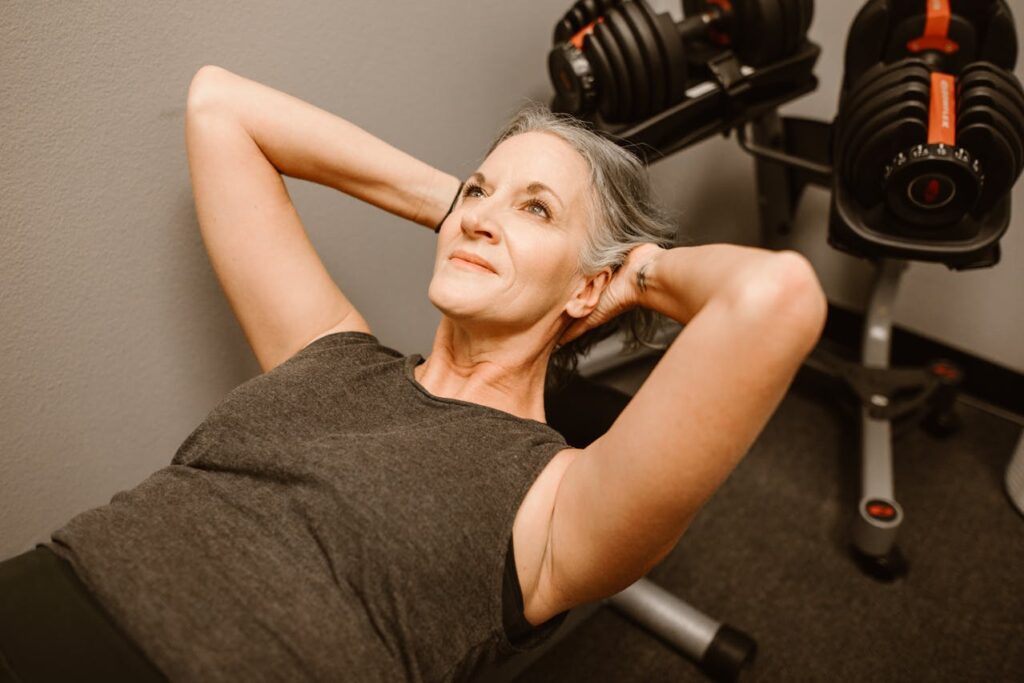 A middle-aged woman with gray hair doing sit-ups in a gym.