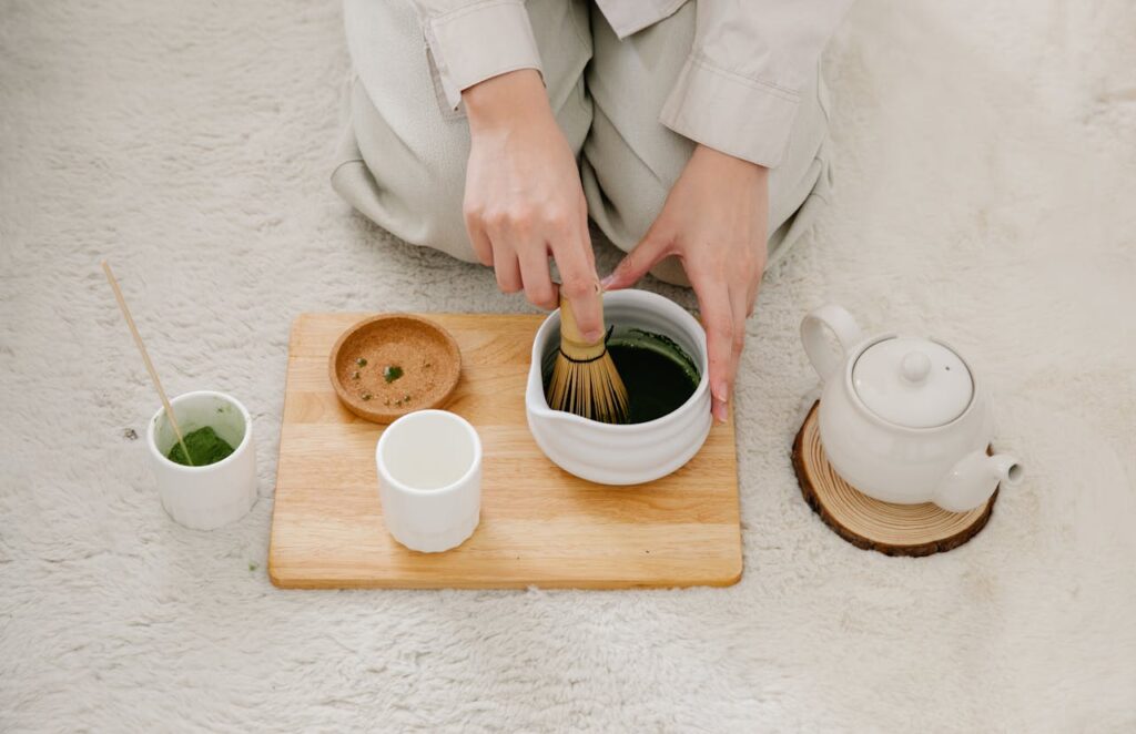 A person using a bamboo whisk to prepare matcha green tea in a ceramic bowl.