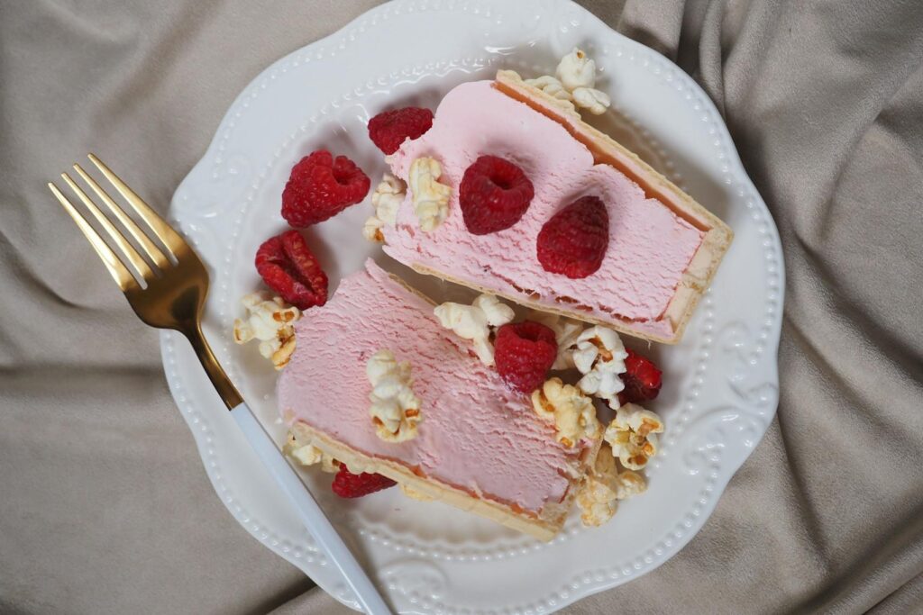 A plate with two slices of raspberry-flavored ice cream dessert, garnished with fresh raspberries and popcorn.