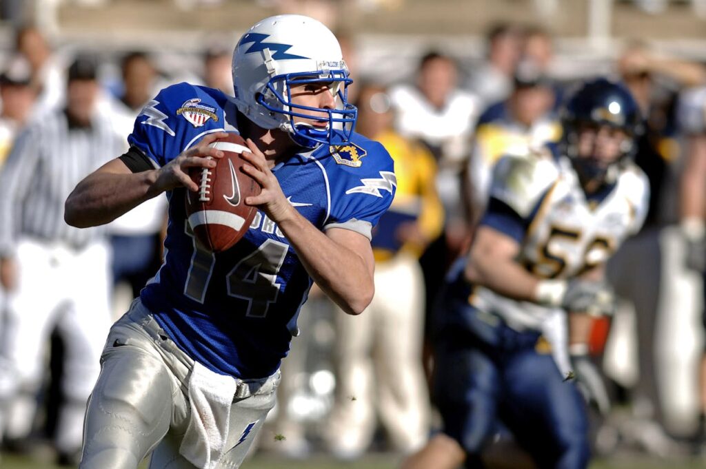 A quarterback in blue uniform holding a football, poised to throw it.