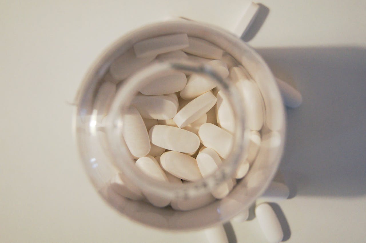 A top-down view of white pill tablets inside and spilling out of a transparent bottle.