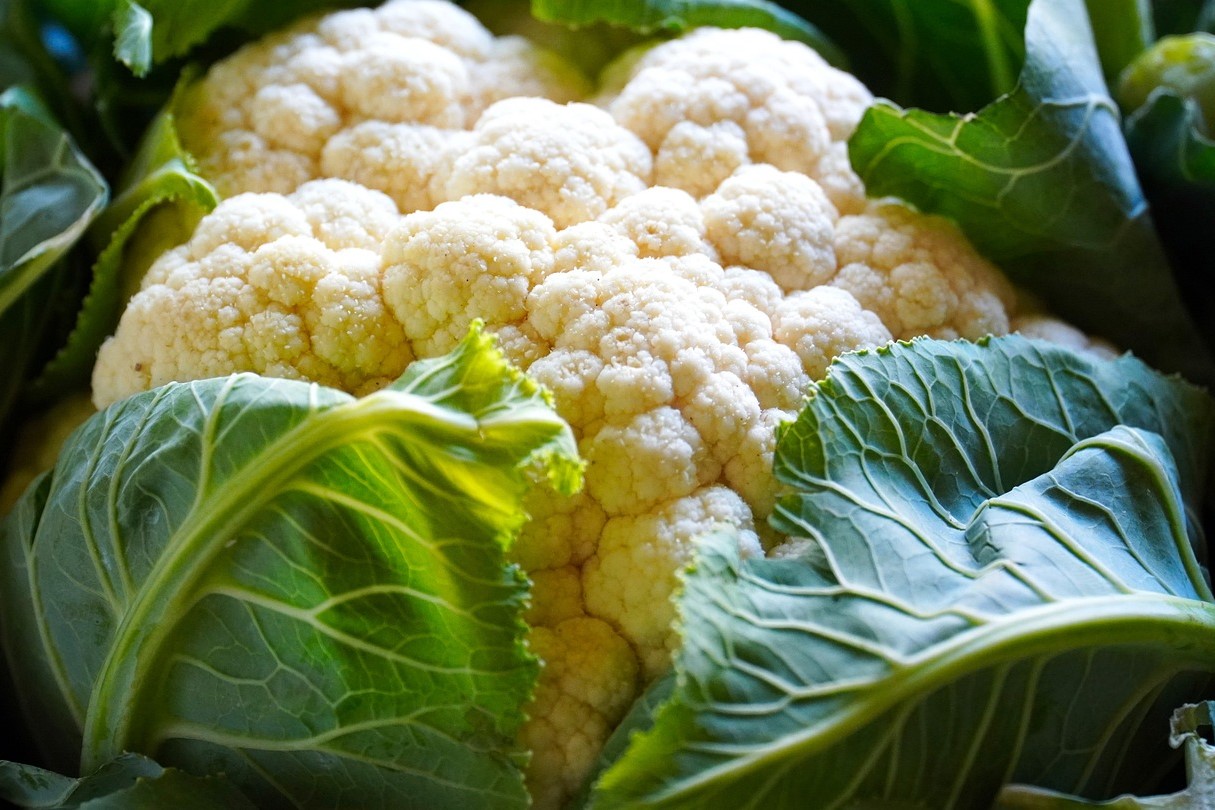 Close-up of fresh cauliflower with green leaves surrounding it.