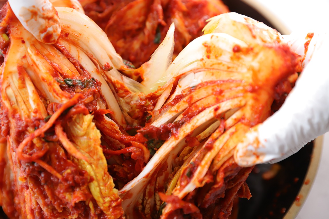 Hands holding a large portion of kimchi cabbage coated with red pepper paste, demonstrating the process of making traditional Korean fermented kimchi.