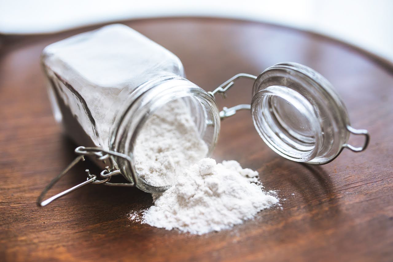 Jar of L-arginine supplement powder spilled on a wooden surface