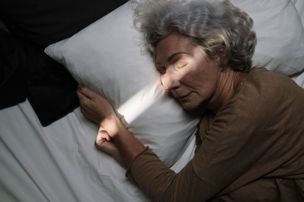 Older woman peacefully sleeping on her side in bed with natural light casting a soft shadow across her face.