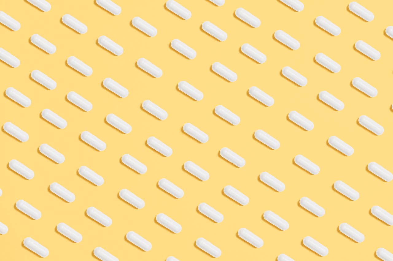 Rows of white capsules arranged diagonally on a yellow background.