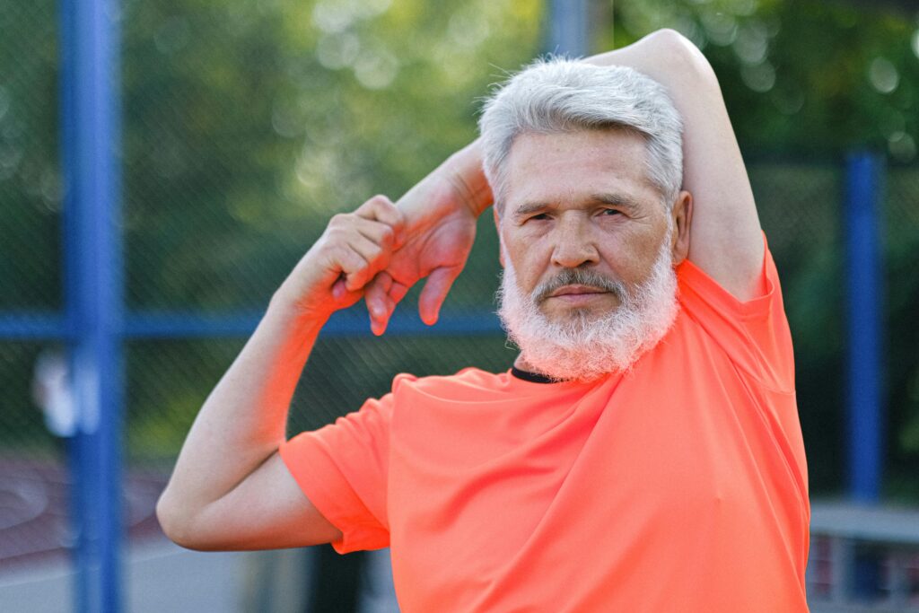 Senior man in orange shirt stretching outdoors.