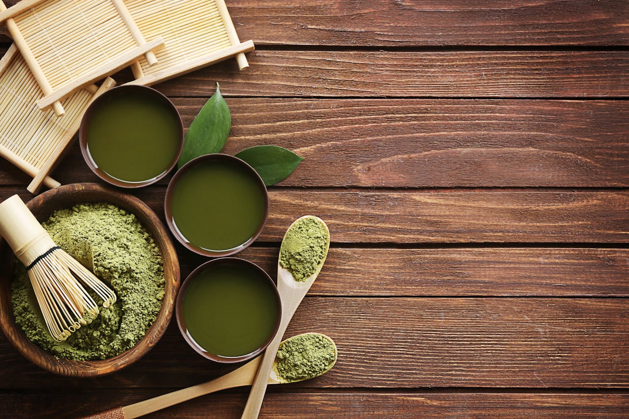Various matcha green tea preparations, including a bowl of matcha powder, a bamboo whisk, and cups of matcha tea.