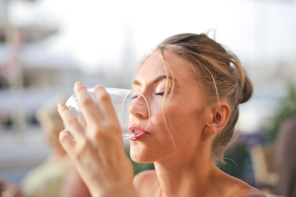 Woman drinking water from a glass with eyes closed.