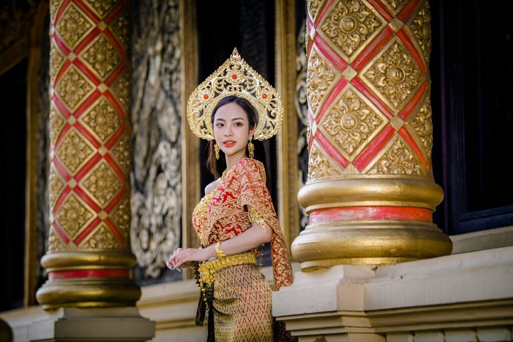 Woman in traditional Thai clothing standing near intricately designed temple pillars.