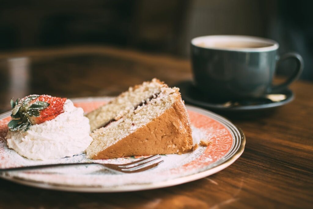 A slice of cake on a plate next to a cup of coffee.
