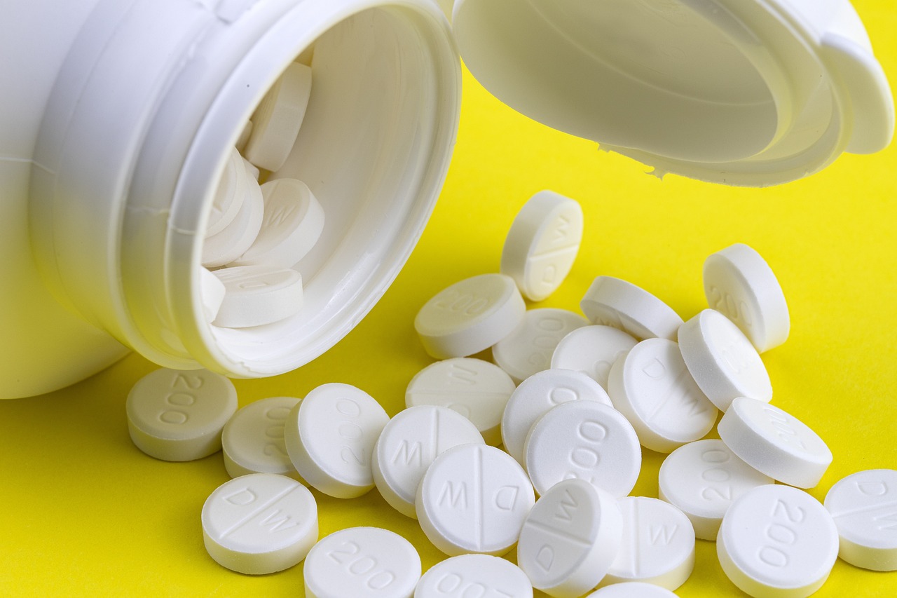 White tablets spilled from a plastic container onto a yellow surface.